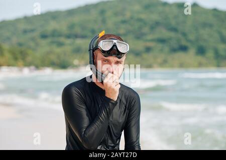 Gutaussehender junger Mann, der nach dem Tauchen im Meer durch den Schnorchel weht Stockfoto