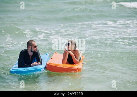 Glücklicher junger Mann und Frau, die sich nach dem Schwimmen im Meerestiergerät in Kunststoffmatratzen ausruhen Stockfoto