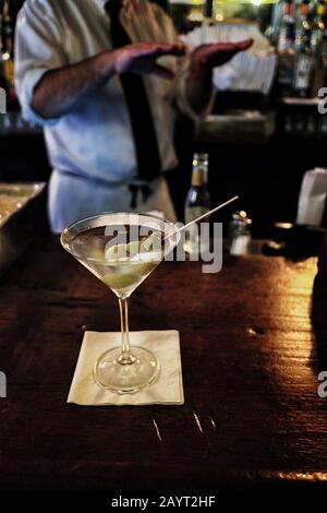 Martini mit drei Oliven an einer alten Holzbar in NYC, die Barkeeper hinter sich Stockfoto