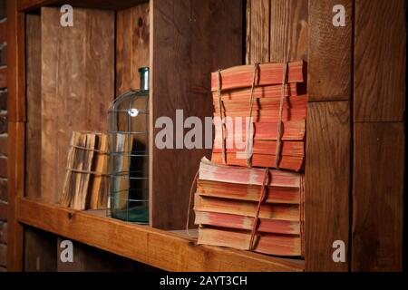 Alte Bücher, mit einem Seil umwickelt, stehen auf einem Holzregal. Neben den Büchern befindet sich eine leere Flasche, die mit einem Seil umwickelt wird.