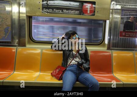 Lifestyle-Reisen - Zeitgenössische asiatische Frau, die beiläufig in einer leeren U-Bahn-Kutsche auf der Linie South Ferry #1 - Manhattan, New York City sitzt Stockfoto