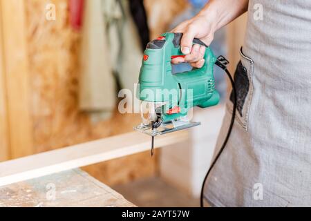 Nahaufnahme des Mitarbeiters, der eine gemusterte Kontur auf einem Holzbrett mithilfe einer elektrischen Stichsäge mit einer Laserführung ausschneidet Stockfoto