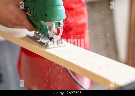 Nahaufnahme des Mitarbeiters, der eine gemusterte Kontur auf einem Holzbrett mithilfe einer elektrischen Stichsäge mit einer Laserführung ausschneidet Stockfoto