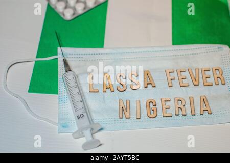 Nigerianische Flagge unter den Worten Lassa Fever Outbreak-Konzept. Atemschutzmaske und Spritze. Lassa hämorrhagisches Fieber LHF endemisch in Westafrika inkl Stockfoto