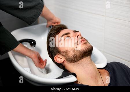 Frau, die Shampoo massiert Haar Kunde Mann waschen Haare im Beauty-Salon Friseursalon waschen Haare. Fröhlicher kaukasischer Kerl genießt Service im Barbersho Stockfoto