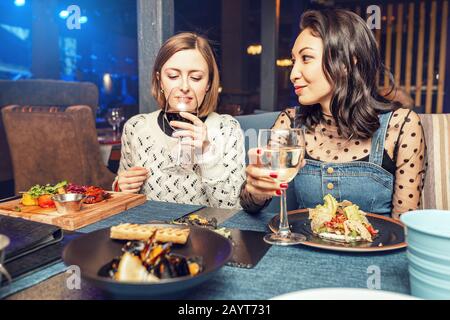 Zwei Mädchen-Freunde unterhalten sich und trinken Wein in einem Restaurant in einem Nachtclub. Freundschaftskonzept, Essen und Getränke Stockfoto