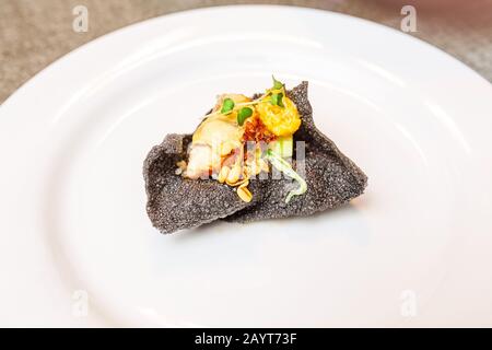 Haute Cuisine Gericht mit Tintenfisch mit Aal und Gemüse auf einem Teller. Kreatives und minimalistisches Delikatessenkonzept Stockfoto