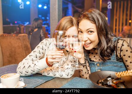 Zwei Freundinnen haben Spaß und unterhalten sich, während sie ein Glas Wein in einem Restaurant in einem Nachtclub trinken. Das Konzept der Entspannung und der Frigschaft Stockfoto