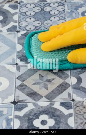 Person, die Gummihandschuhe trägt, die mit einem Schwamm verzierte blaue und weiße Fliesen auf einer Arbeitsplatte in der Küche reinigen. Stockfoto