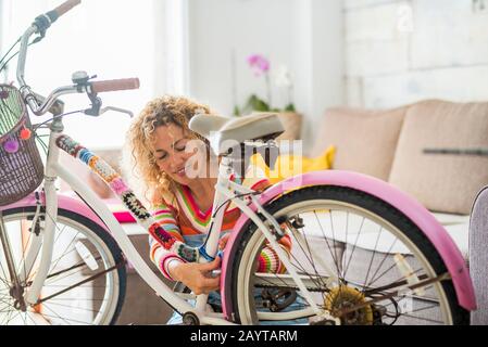 Schöne kaukasische junge Frau, die zu Hause ein Fahrrad mit handgefertigten Schneiderkunstmaterialien - Menschen und Farben mit verrücktem Kunst-Lebensstil - modifizieren kann, ist glücklich Stockfoto