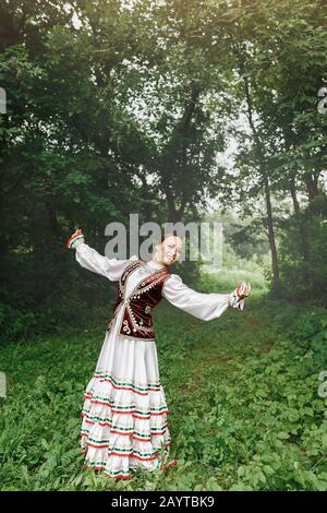 Eine Frau in traditioneller, gestickter Turkostkleidung führt im Park einen Nationaltanz aus Stockfoto