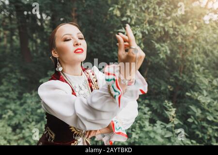 Eine Frau in traditioneller, gestickter Turkostkleidung führt im Park einen Nationaltanz aus Stockfoto