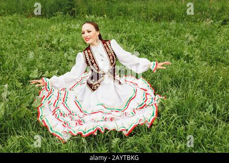 Eine Frau in traditioneller, gestickter Turkostkleidung führt im Park einen Nationaltanz aus Stockfoto