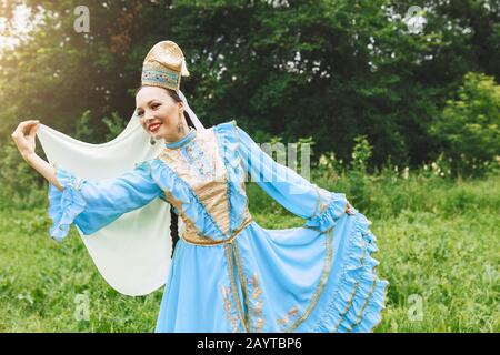 Eine Frau in traditioneller, gestickter Turkostkleidung führt im Park einen Nationaltanz aus Stockfoto