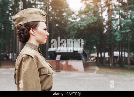 Ein Mädchen in einer alten sowjetischen Militäruniform grüßt im Parkdenkmal mit Panzer T-34 am Hintergrund. Der Sieg im zweiten Weltkrieg feiert am 9. Mai in Russland Stockfoto