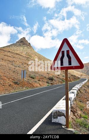 Dreikantige Straßenverengung auf der Bergstraße mit Berg im Hintergrund. Die Straße geht deutlich von zwei Spuren auf einspurige Strecke. Stockfoto