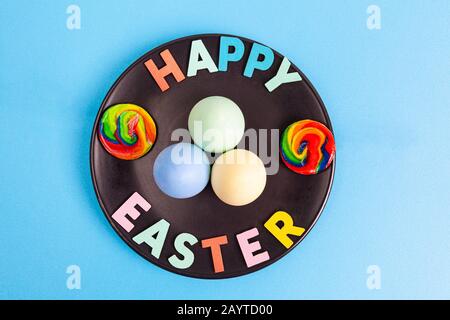 Fröhlicher Ostertext mit bunten Eiern und auf schwarzem Teller angeordneten Marshmallows Stockfoto