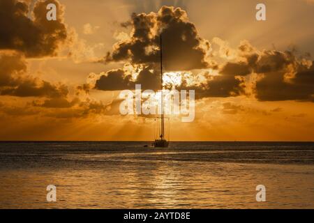 Blick auf den Sonnenuntergang auf die Yacht, die in der Lagune, der Bucht von Britannia, der Insel Mustique, Saint Vincent und die Grenadinen, dem karibischen Meer, verankert ist Stockfoto