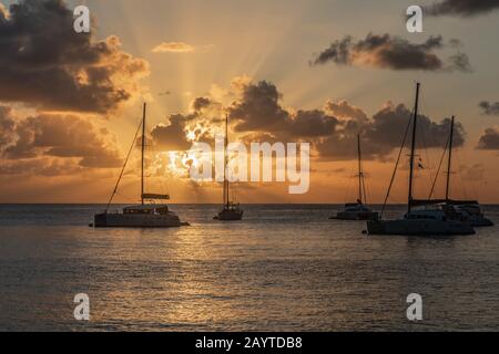 Blick auf den Sonnenuntergang von Yachten und Katamaranen, die in der Lagune, der Bucht von Britannia, der Insel Mustique, Saint Vincent und die Grenadinen, dem karibischen Meer, verankert sind Stockfoto
