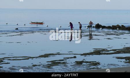 Banay Banay, Davao Oriental, Philippinen - März 2016: Drei Menschen spazieren bei Ebbe am frühen Morgen auf den südlichen Philippinen am Strand. Stockfoto