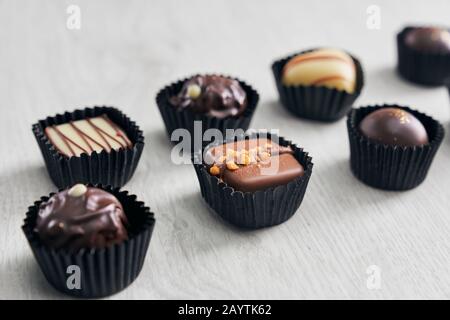 Verschiedene köstliche Schokoladenkäuze mit unterschiedlicher Form und Farbe in Verpackungspapier über rustikalem Holzhintergrund. Luxus-Sortiment für leckeren Genuss. Stockfoto