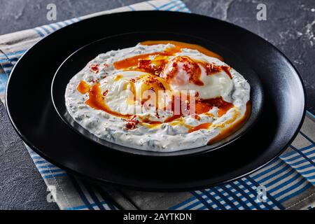 Nahaufnahme von Cilbir, pochierten Eiern in Joghurt, mit würziger, aufgeschäumter Butter, serviert auf schwarzen Tellern mit goldenem Besteck, türkischer Küche, Horizon Stockfoto