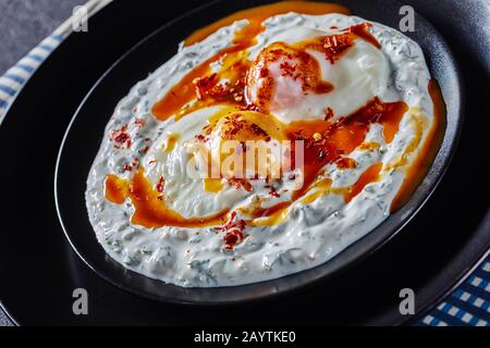 Nahaufnahme von cilbir, pochierten Eiern in Joghurt, mit würziger, aufgeschäumter Butter, die auf schwarzen Tellern serviert wird Stockfoto