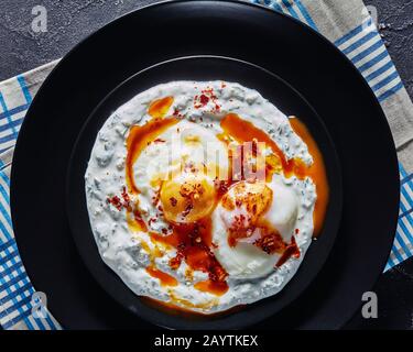 Cilbir, pochierte Eier in Joghurt Soße mit würziger, auf schwarzen Tellern aufgeschäumter Butter, türkische Küche, horizontaler Blick von oben, flacher Lay, c Stockfoto