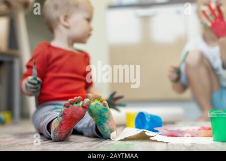 Hübsche süße kaukasische kleine blonde Geschwister Kinder genießen Spaß beim Malen mit Pinsel und Handfläche zuhause. Fröhliche glückliche Kinder lächeln Stockfoto