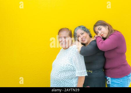 Großmutter, Tochter und Enkelin ruhen auf ihren Schultern und schauen auf die Kamera, drei Generationen mexikanischer Frauen lächeln in legerer Cloo Stockfoto