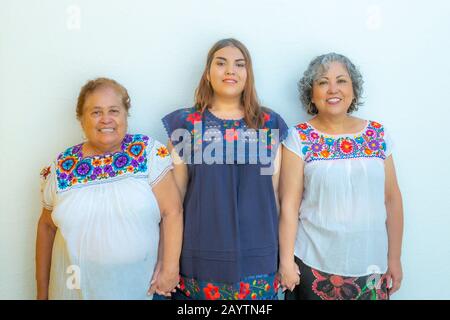 Drei Generationen lateinmexikanischer Frauen lächeln, Großmutter, Enkelin und Tochter mit geblümten Blusen, die Hände halten, die auf die Nocken blicken Stockfoto