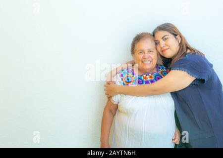 Enkelin umarmte ihre Großmutter, zwei lächelnde mexikanische Frauen auf weißem Hintergrund, Platz für Text Stockfoto