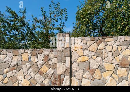 Exquisiter Steinzaun vor dem Hintergrund eines Sommergartens Stockfoto