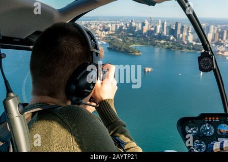 Sydney, Australien - 18. Juni 2014: Kaukasischer Mann fotografiert mit dem Hubschrauber das CBD von Sydney und den Hafen von Sydney. Tourist vor dem Sitz im Hubschrauber p Stockfoto