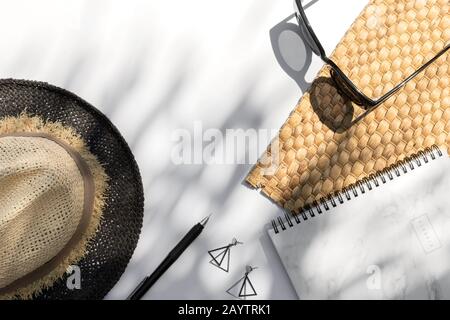 Trendige Sonnenbrille, Planer, Hut, Ohrringe mit Palmblattschatten auf weißem Hintergrund Stockfoto