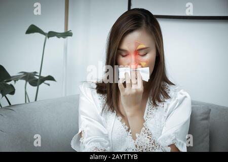Asiatische Frauen tragen weiße Nachtgown- und langärmlige Satin-Robe mit Blumenspitze und fühlen sich nachts sinusitis an. Ein Mädchen leidet im Wohnzimmer unter Sinus. Stockfoto