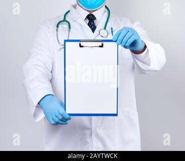 Hausarzt in einem weißen Mantel, blaue Latexhandschuhe, ein Stethoskop, das an seinem Hals hängt und einen Papierhalter mit einem weißen leeren Blatt hält, Platz zum Schreiben eines Stockfoto