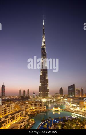 Der Burj Khalifa und die Innenstadt Dubais werden bei Sonnenuntergang beleuchtet, während Touristen auf die Spekatulr-Show des Dubai-Brunnens warten. Stockfoto