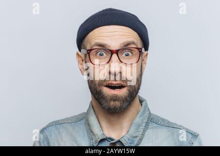 Horizontale Schuss überrascht, schockiert Mann starrt Kamera mit unerwarteter Ausdruck begeistert, hält den Mund öffnete, hört schreckliche Nachrichten, über Graues ba isoliert Stockfoto