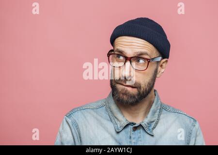 Portrait von unrasiert nachdenkliche Männer mittleren Alters mit nachdenklichen Ausdruck sieht nach oben, trägt stylischen Hut, Brillen und Jeansjacke, über dem Stift isoliert Stockfoto