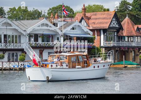 Der klassische Kabinenkreuzer oder die Motoryacht "Nodens" aus dem Jahr 1965 passiert Häuser am Flussufer der Themse bei Henley-on-Thames Stockfoto