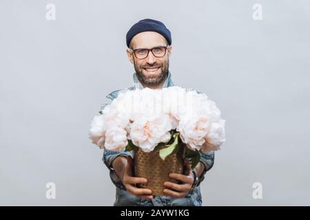 Diese Blumen sind für Sie! Froh lächelnde bärtigen Mann erstreckt sich Hände beim Bündel von weißen Blumen hält, macht heute für jemanden, isoliert Stockfoto