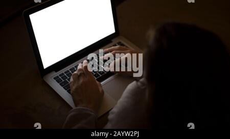 Paarbeziehungen und Dating im modernen Zeitkonzept: Nahaufnahme der Hände der Frau beim Tippen auf der Laptop-Tastatur mit weißem Bildschirm bei schwachem Licht Stockfoto