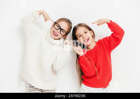 Hey, sieh mal bei uns, wir sind cool! Gerne kleine weibliche Kinder in warmen gestrickten Pullover, machen, Grimasse und lustige Ausdrücke, über weiß Hinterg isoliert Stockfoto