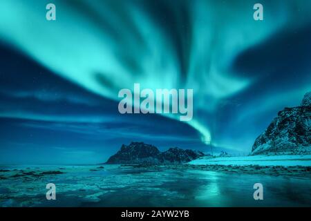 Aurora borealis über die verschneiten Berge und den sandigen Strand Stockfoto