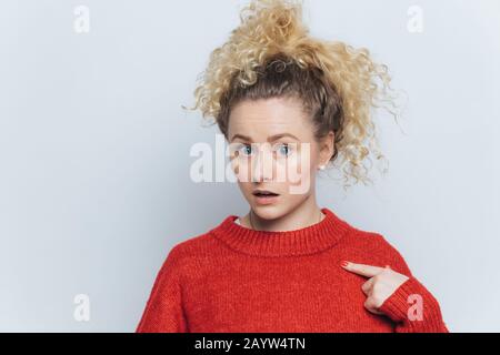 Schöne, verblüffte junge Frau mit schockierter, unerwarteter Ausdrucksweise, zeigt mit dem Zeigefinger an ihrem neuen roten Pullover Platz für Ihre Werbung. Stockfoto
