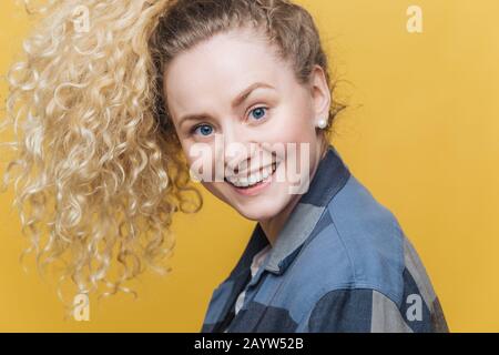 Seitlicher Schuss von einem entzückenden jungen Frauenmodell mit lockigen Haaren, breitem strahlendem Lächeln, genießt Freizeit bei engen Menschen, gerne Tag für Tag. Stockfoto