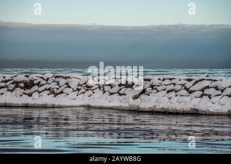 Felsen auf dem Pier, bedeckt mit Schnee und Eis. Wellenbrecher in der Ostsee an einem bewölkten kalten Tag. Stockfoto