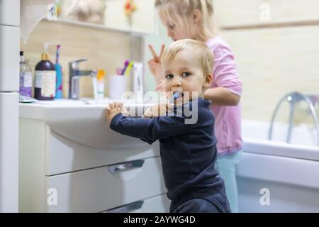 Zwei süße, hübsche blonde, kaukasische Geschwister, die morgens im Bad das Gesicht waschen und den Zahn mit Zahnbürste reinigen. Kleine Kinder Bruder und Stockfoto