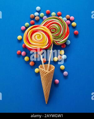 Festliche Party-Candy-Stillleben mit Spirallollipops umgeben von bunten, zuckerbeschichteten Schokoladenbonbons auf blauem Hintergrund Stockfoto